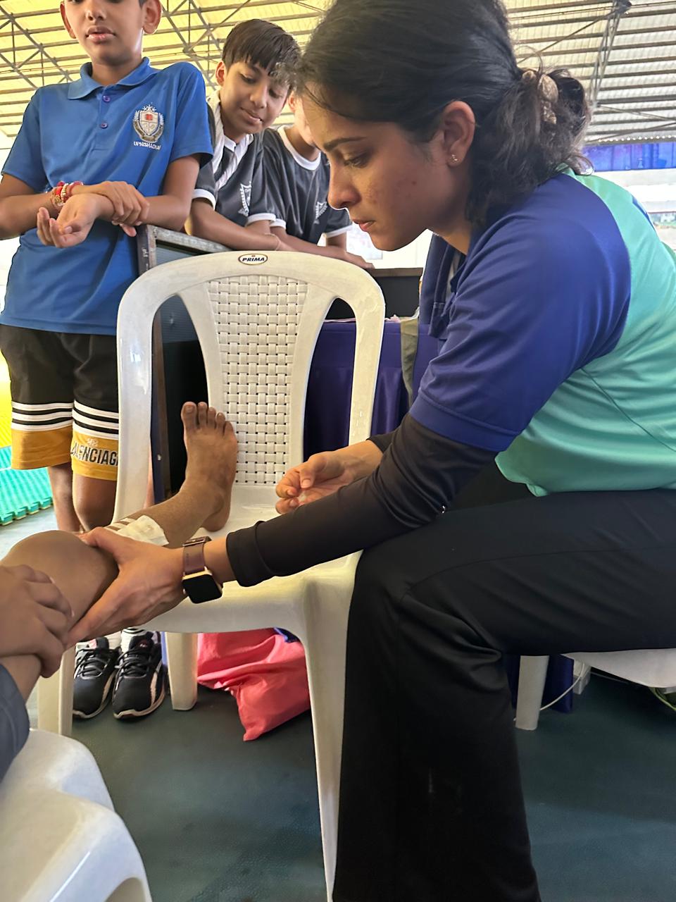 Dr. Vedika Gujarathi treating a young athlete's ankle inside a sports hall.