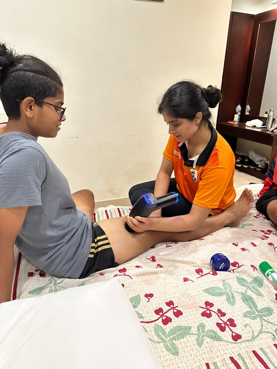 Percussion massage gun applied to an athlete's leg during a recovery session.